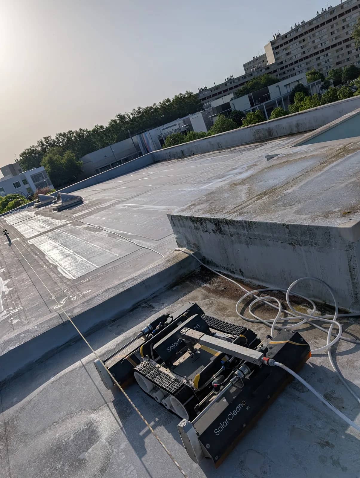 Robot à chenilles SolarCleano M1 et son tuyau au bord d'une toiture plate en béton